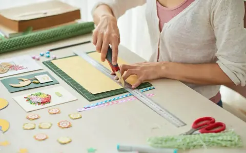 Tworzenie zaproszenia na urodziny: ręce tną papier z linijką, obok ozdoby i nożyczki.