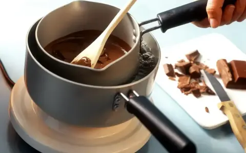 Delikatne topienie czekolady w kąpieli wodnej, by uzyskać idealną konsystencję. Drewniana łyżka miesza płynną masę.