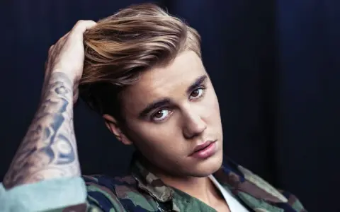 Justin Bieber mit tätowiertem Arm und Camouflage-Jacke, blickt in die Kamera.