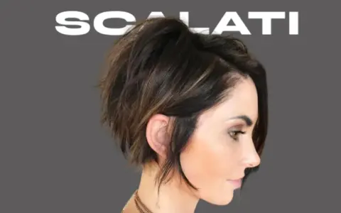 Modello con un audace taglio scalato medio corto, che incornicia il viso con ciocche texturizzate e un tocco di balayage.