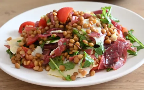 Insalata di lenticchie con pomodorini, scaglie di parmigiano e prosciutto crudo, un piatto fresco e gustoso.