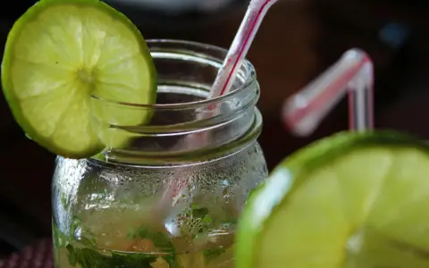 Orzeźwiający mohito drink, z widocznymi składnikami: limonką i miętą, w szklanym słoiku z rurką.