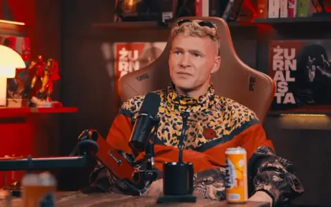 Mężczyzna w kurtce w panterkę, z blond włosami, siedzi w fotelu. Na półce za nim figurki Iron Mana. Wiek majora SPZ.