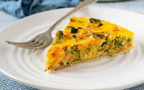 Rebanada de quiche vegetal con brócoli y zanahoria, servida en plato blanco con tenedor.