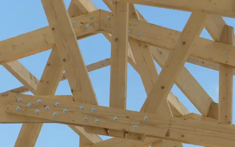 Assemblage ferme charpente en bois, structure solide sous un ciel bleu.