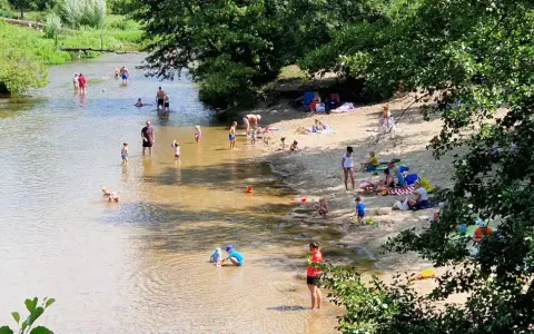 Słoneczny dzień nad Świdrem. Ludzie odpoczywają na piaszczystej plaży i kąpią się w rzece. Dzieci bawią się w wodzie.