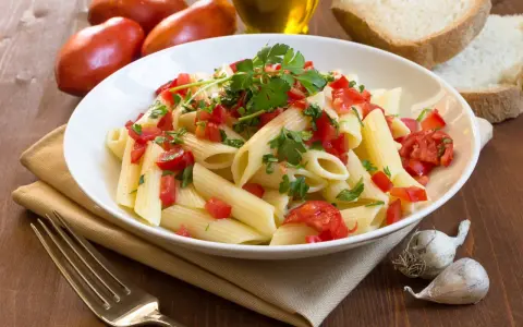 Świeży makaron penne z pomidorami i pietruszką, obok chleb, czosnek i oliwa. Porównanie makaronu świeżego z lodówki kontra suchego z paczki.