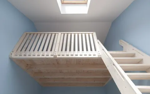 Jasna, drewniana antresola z balustradą i schodami, podświetlona przez okno dachowe.