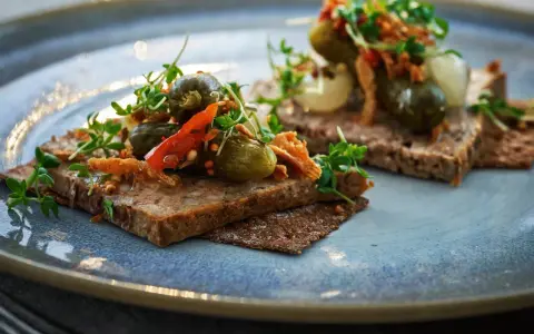 Två bitar mörkt bröd med leverpastej, toppade med cornichoner, chili och krispiga topping. Ett enkelt leverpastej recept att inspireras av.