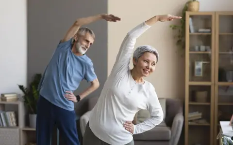 Uśmiechnięta para seniorów ćwiczy w domu. Aktywne zajęcia dla seniorów to świetny sposób na zdrowie i dobre samopoczucie.