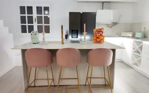 Elegantes cocinas con isla, tres taburetes rosas y dorados invitan a disfrutar.