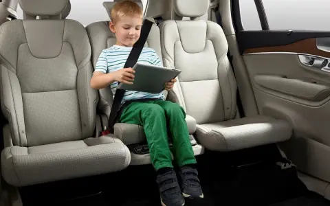 Niño en asiento elevador integrado, con cinturón de seguridad puesto, usando una tablet. ¿Cuál es el asiento más seguro del coche?