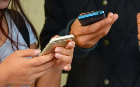 Zwei Hände halten Smartphones. Eine Frau hält ein goldenes iPhone, ein Mann ein blaues Handy. Vielleicht kommen eingehende Anrufe nicht an.