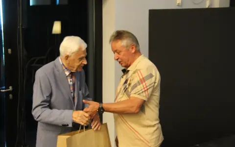 Zdzisław Kuźniar syn, starszy pan w niebieskiej marynarce, wręcza prezent młodszemu mężczyźnie w beżowej koszulce.