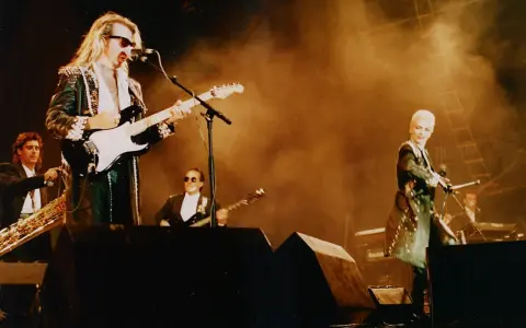 Medlemmar av Eurythmics på scen. Dave Stewart spelar gitarr, Annie Lennox sjunger. En saxofonist och en keyboardist syns också.