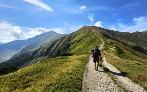 Wędrowiec na szlaku prowadzącym na Starorobociański Wierch. Zielone zbocza gór i błękitne niebo z chmurami.