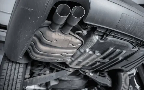 The underside of a car shows a dual exhaust system leading to a large muffler, which is a key component for reducing engine noise.