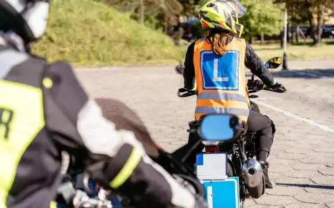 Rozpoczyna się kurs na motocykl. Uczestnicy w kamizelkach z literą "L" ćwiczą jazdę na placu manewrowym.