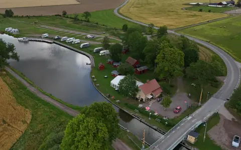Jonsboda camping vid en kanal med husbilar, båtar och röda stugor. En bro leder över vattnet.