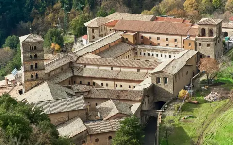 Aerial view of a sprawling monastery complex near Rome, with terracotta roofs and a tall bell tower.