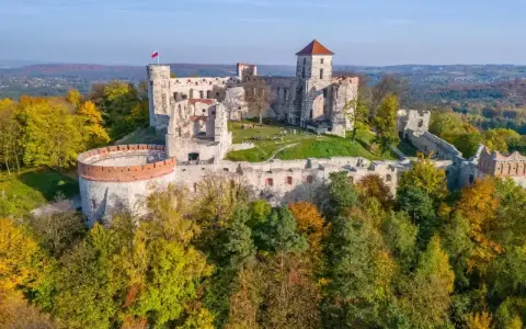 Ruiny zamków Jury Krakowsko-Częstochowskiej na tle jesiennych lasów. Majestatyczne kamienne mury i wieże, polska flaga powiewa na wietrze.