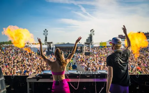 DJ-ka i DJ na scenie, płomienie buchają, tłum szaleje na festiwalu muzyki elektronicznej.