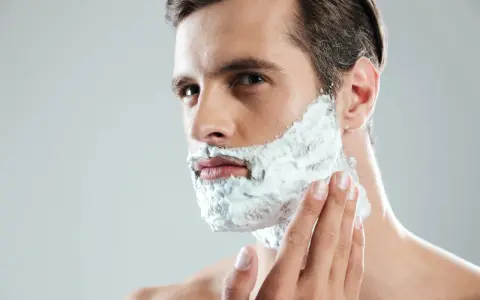 Hombre aplicándose espuma para afeitarse sin espuma. Su mano acaricia su mejilla mientras se prepara para un afeitado apurado.
