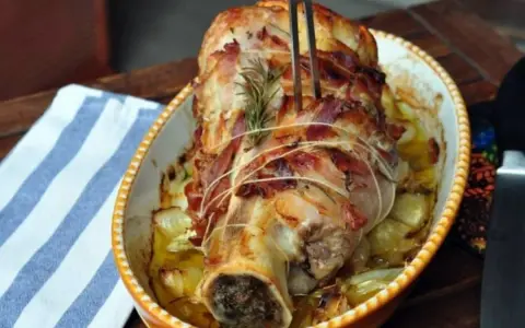 Stinco di vitello al forno, avvolto in pancetta e cotto con cipolle e rosmarino, pronto per essere servito.