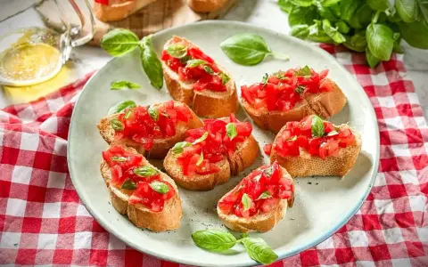 Frische Crostini Variationen mit Tomaten und Basilikum auf einem Teller, garniert mit frischen Basilikumblättern.