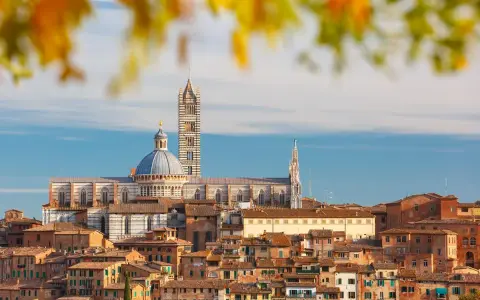 Vue panoramique de la ville de Sienne, avec sa cathédrale imposante et ses toits de tuiles ocres, baignée par la lumière dorée de la terre de sienne.