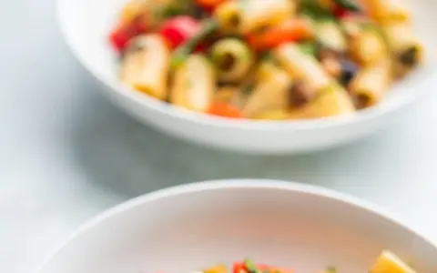 Due ciotole bianche piene di pasta con verdure colorate, un piatto estivo invitante.
