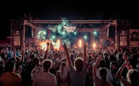 Multitud en concierto bajo luces y humo, con cartel de "Venice Bay" y "Sonorama Ibiza".