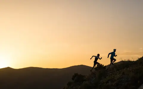 Dos corredores se enfrentan a una exigente carrera de senderos al amanecer, sus siluetas recortadas contra un cielo anaranjado.