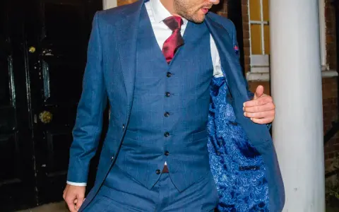 A man in a blue checkered suit, white shirt, and red tie. He's showing off the paisley lining of his jacket, and the bottom button on his vest is unbuttoned.