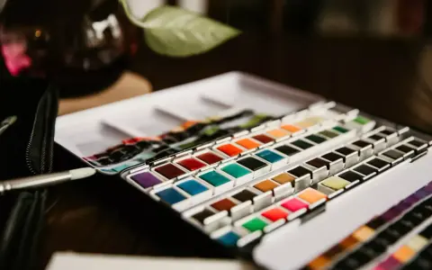 Une palette de matériel peinture aquarelle aux couleurs vives, prête à l'emploi. Un pinceau est posé à côté.