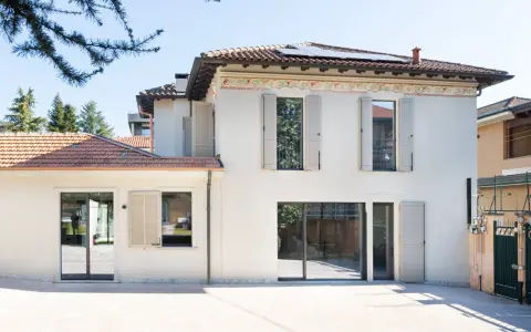 L'abbinamento colori facciata e serramenti crea un'armonia moderna. La casa bianca con dettagli decorativi si fonde con le persiane e gli infissi grigio chiaro.
