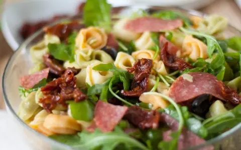 Kolorowa sałatka z tortellini, rukolą, suszonymi pomidorami i salami. Idealna na letni obiad.