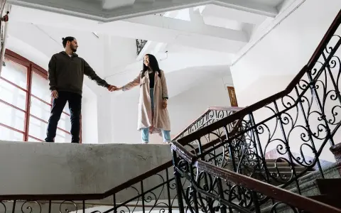 Pareja tomados de la mano en una escalera, ¿qué es ser posesivo? Él la mira, ella sonríe.