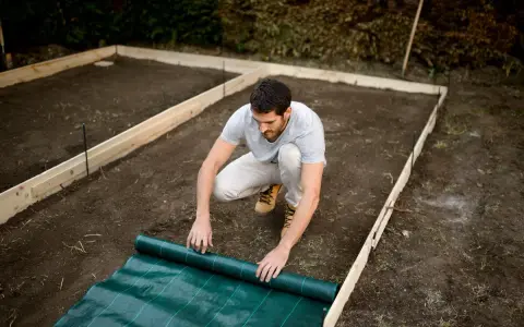 Hombre desplegando tela verde sobre el terreno preparado para una solera de hormigón.