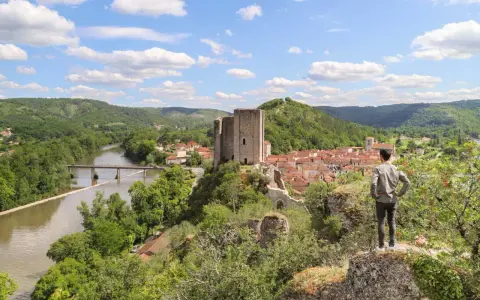 Un homme admire un village médiéval avec un château, un fleuve et des collines verdoyantes, un aperçu du circuit des plus beaux villages du Lot.