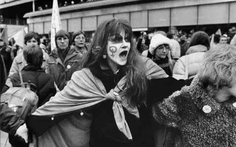 En kvinna med ansiktsmålning och symbolen för kvinnor ropar under en demonstration för sveriges demokratisering.