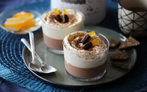 Deux verrines 3 chocolat, garnies de crème fouettée, de copeaux de chocolat et d'écorces d'orange confites.