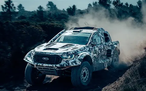 Un Ford Raptor Dakar camuflado levanta polvo en un terreno agreste.