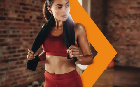 Donna sudata in abbigliamento sportivo rosso, con un asciugamano nero, si riposa dopo l'allenamento. Con il caldo i battiti aumentano, ma lei è determinata.