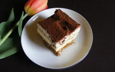 Pyszny kawałek tiramisu, jednego z 10 ciast bez pieczenia, obok czerwonego tulipana.