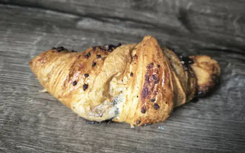 Chrupiący croissant z kawałkami czekolady na drewnianym tle. Idealny na śniadanie, choć warto sprawdzić jego kcal.