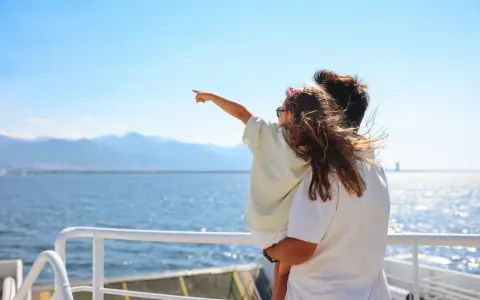 Bambina indica l'orizzonte da una nave, con la famiglia in vacanza a Favignana. Il mare azzurro e le montagne sullo sfondo creano un'atmosfera serena.