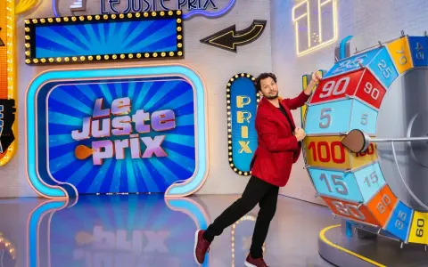 Un animateur pose près de la roue du jeu "Le Juste Prix". L'illustration du plateau est colorée et lumineuse, promettant de beaux gains.