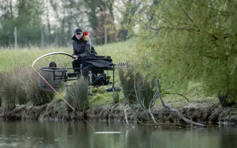 Wędkarz przygotowuje zestaw na sandacza z gruntu. Widać wędkę, podbierak i skrzynkę wędkarską.