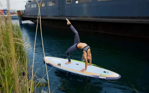 Frau macht Yoga-Brücke auf SUP-Board. Stand up paddle gesund und fördert Balance.